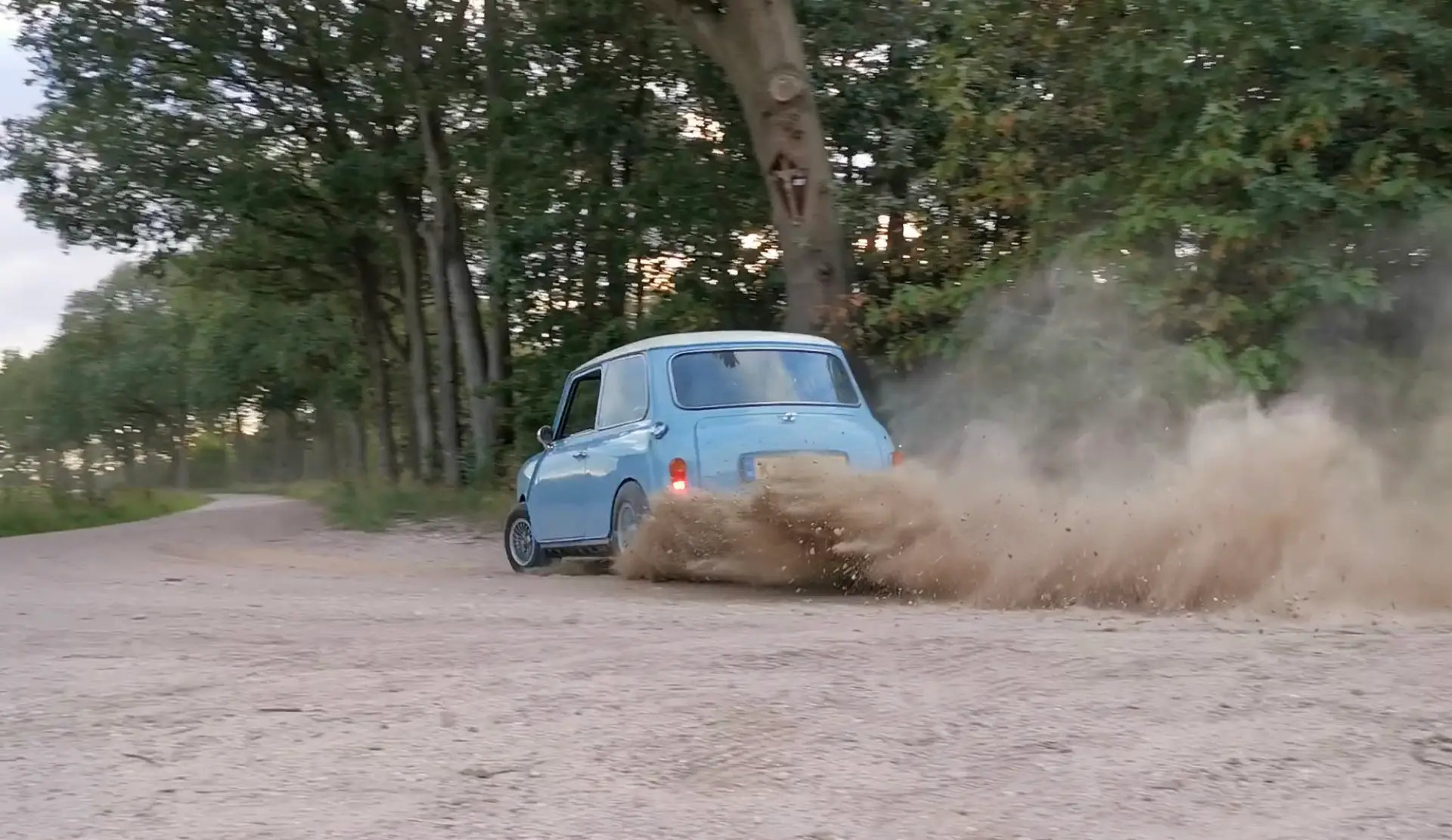Een crossende lichtblauwe Austin Mini dat slipt in de bocht van een grindpad